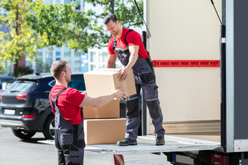 Two Young Male Movers Carrying Cardboard Boxes From Truck