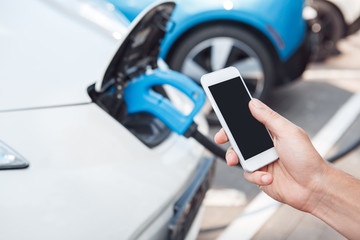 Young adult man using smartphone and paying for charging electric car