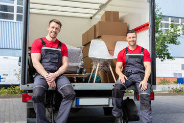 Portrait Of Smiling Movers Sitting In Truck With Moving Boxes
