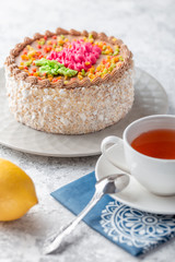 Sponge biscuite cake with cream lies on a plate. On the table are berries, a cup with tea and a spoon, a napkin.