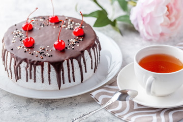 Sponge biscuite cake with cream lies on a plate. On the table are berries, a cup with tea and a spoon, a napkin.
