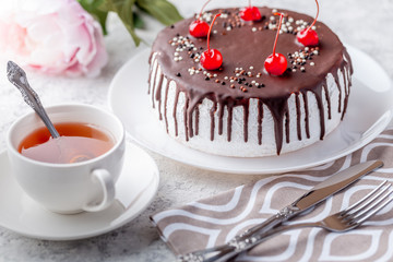 Sponge biscuite cake with cream lies on a plate. On the table are berries, a cup with tea and a spoon, a napkin.