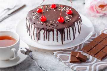 Sponge biscuite cake with cream lies on a plate. On the table are berries, a cup with tea and a spoon, a napkin.