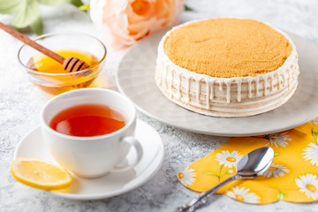 Sponge biscuite cake with cream lies on a plate. On the table are berries, a cup with tea and a spoon, a napkin.