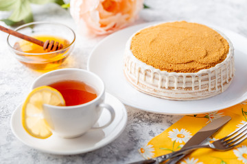 Sponge biscuite cake with cream lies on a plate. On the table are berries, a cup with tea and a spoon, a napkin.