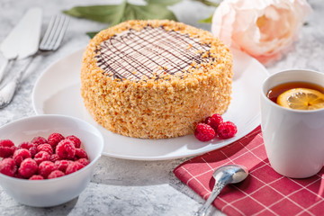 Sponge biscuite cake with cream lies on a plate. On the table are berries, a cup with tea and a spoon, a napkin.