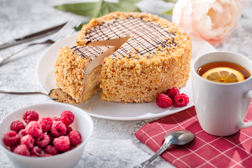 Sponge biscuite cake with cream lies on a plate. On the table are berries, a cup with tea and a spoon, a napkin.