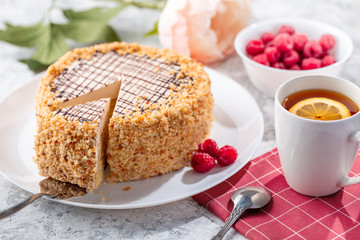 Sponge biscuite cake with cream lies on a plate. On the table are berries, a cup with tea and a spoon, a napkin.