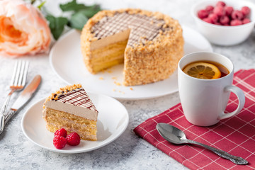 Sponge biscuite cake with cream lies on a plate. On the table are berries, a cup with tea and a spoon, a napkin.