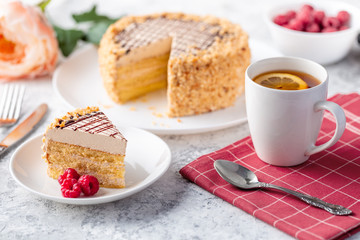 Sponge biscuite cake with cream lies on a plate. On the table are berries, a cup with tea and a spoon, a napkin.