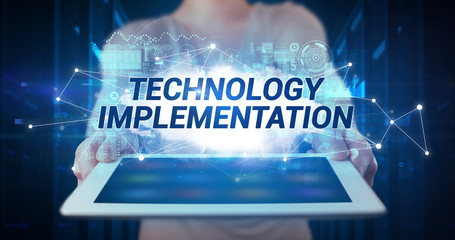 Young business person working on tablet and shows the inscription: TECHNOLOGY IMPLEMENTATION