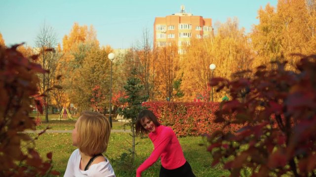 Sporty smiling women dancing in autumn park. Beautiful happy flexible women in sportswear exercising together and dancing on meadow in park