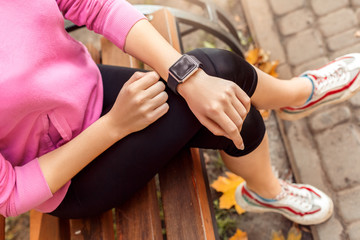Fototapeta premium Healthy Lifestyle. Young woman sitting on bench outdoors autumn season checking time on watch top view