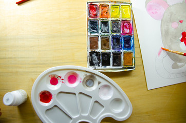 Girl sitting draws with watercolors on a white sheet of paper a mouse with a green gift. Top view. New Year 2020, the year of the mouse