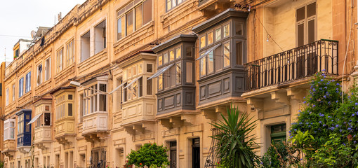 Fototapeta na wymiar Residential house facade with traditional Maltese wooden balconies in Sliema, Malta, coloured in orange with evening sunlight. Authentic Maltese urban scene.