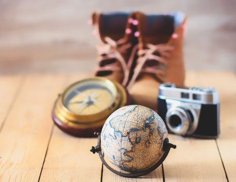 GLOBE, CAMERA OF PHOTOS AND BOOTS ON WOODEN TABLE. TRAVEL COMPLEMENTS