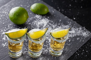 Three glasses of golden Mexican tequila and lime with salt