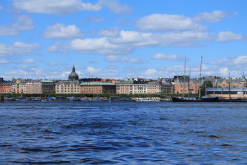 City houses on a background of sea water and a cloudy sky. Buildings are located in the center of the frame, in front - water. View from the sea.