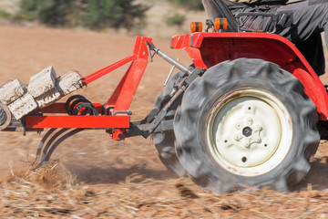 Red Tractor With Plough Plowing Field Soil Close Up View .