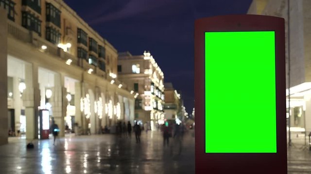 Modern billboard with a green screen on a busy night street with crowds of people, timelapse of walking area