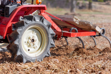 Red Tractor With Plough Plowing Field Soil Close Up View .