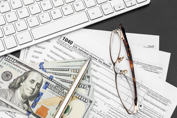 Tax forms with money, glasses and computer keyboard on black. Top view.