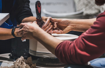 A master behind a pottery wheel teaches a student in a ceramic workshop. Pottery training.