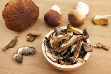 Dried mushrooms in a bowl surrounded by freshly picked boletus