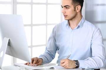 Businessman working with computer in modern office. Headshot of arab male entrepreneur or manager at workplace. Business concept