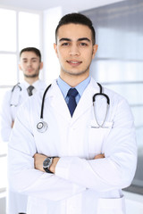 Arab doctor man standing with caucasian colleague in medical office or clinic. Diverse doctors team, medicine and healthcare concept