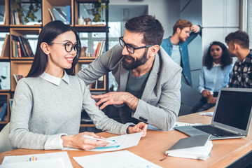 Startupers working together at office woman in eyeglasses sitting talking with colleague about document happy