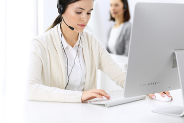 Call center. Beautiful woman receptionist sitting in headset at customer service office. Group of operators at work. Business concept
