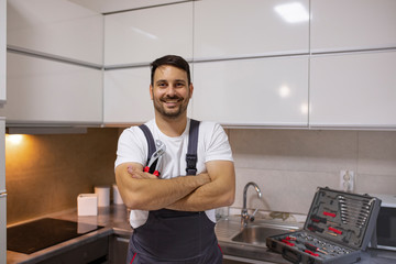 Space for text. Young worker with tool bag standing near oven in kitchen. Portrait of a handyman in uniform standing in the renovated kitchen at home