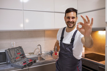 Smiling handsome plumber standing with crossed arms and looking at camera in kitchen. Portrait of a repairman on the kitchen. Service Industry: Mid-adult repairman working at customer's home.