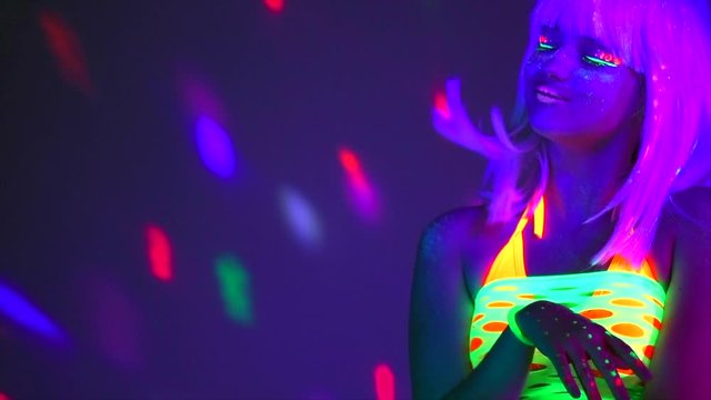 Young woman dancing. Sexy woman posing in neon light. Portrait of beautiful model with fluorescent makeup on bright background. Slow motion 4K UHD video footage. 3840X2160