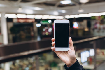 Hand using smartphone for doing business or banking or buying online on blur shopping mall background