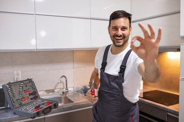  Space for text. Young worker with tool bag standing near oven in kitchen. Portrait of a handyman...