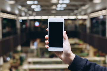 Hand using smartphone for doing business or banking or buying online on blur shopping mall background