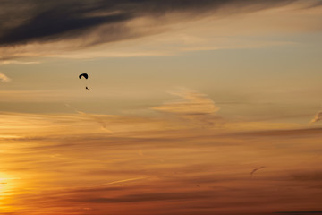 Skydiver flying in the evening sunset sky on a paraglider. There are Cirrus clouds in the sky. The sky is painted orange by the setting sun. Sports, Hobbies and passion. Background or backdrop.