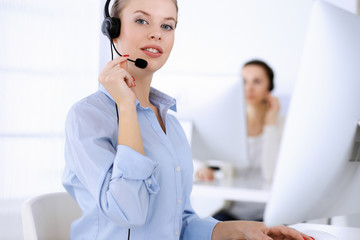 Call center office. Beautiful blonde woman using computer and headset for consulting clients online. Group of operators working as customer service occupation. Business people concept