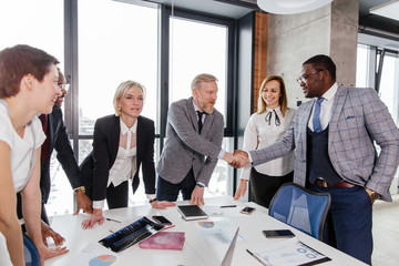 Businessmen of different ages shake hands with African partners standing at the table in the office