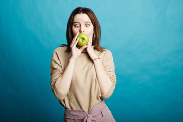 Fototapeta premium Image of a happy young girl standing on a blue background holding a green apple