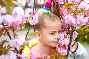 Obraz na płótnie Canvas Smiling blonde girl standing in a blooming garden. Blooming cherry. Portrait of beautiful little girl. Close up of little model face. Sakura blooming, spring time.