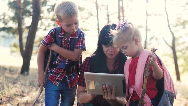 happy family little boy and girl scout navigation tourists teamwork slow motion video concept. mom son and daughter hiking in the forest looking for a way on a digital tablet. group lifestyle of