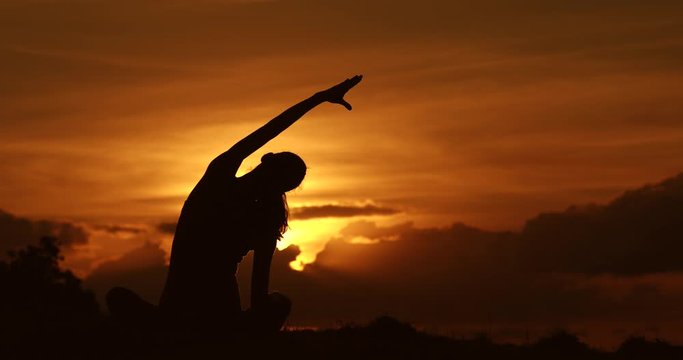Female silhouette doing stretching exercise with beautiful sunrise background. Active healthy lifestyle.