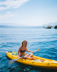 Beautiful caucasian girl paddling a yellow kayak in the mediterranean sea picking up trash and...