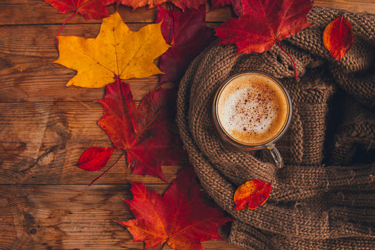 Autumn, fall leaves, hot cup of coffee and a warm wool scarf on wooden table background top view. Seasonal, morning coffee. Hot drink for autumn cold rainy days.