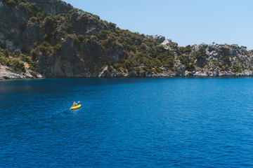Fototapeta na wymiar A lone girl paddling a yellow kayak in remote mediterranean waters, exploring the Turkish coastline. Beautiful blue water and coastline with amazing visibility. Shot aerially with a drone.