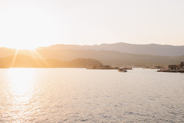 The sun setting over a quiet bay near Fethiye, Turkey. The traditional Turkish gulets line the shore with the mountainous coastal landscape in the background. 