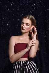 Fashionable girl with bright, professional evening make-up. Burgundy lipstick, clean, natural face, French manicure. Hair is parted, large hanging gold earrings with pearls. Shiny blue background